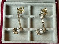 Front view of both silver-tone rhinestone music note brooch pins in case