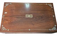 Closed writing slope top showing wood grain and brass/mother-of-pearl inlay with small veneer loss