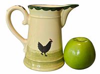 Front view of ceramic jug with chicken motif beside apple for scale