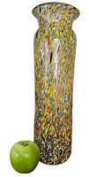 Full view of tall multicolour splatter glass vase beside apple for scale
