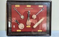 Front view of framed shadow box displaying six miniature instruments on red background