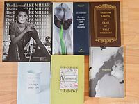 Six hardcover books arranged on wooden surface showing front covers