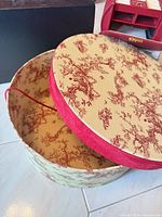 interior and lid of round hat box showing cream base and red toile pattern