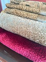 Stacked view of burgundy throw beneath two beige animal-print pieces
