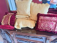 Group of gold coverlet, gold shams and burgundy velvet pillows on dresser