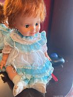 Full view of doll seated wearing blue and white dress, showing face and outfit