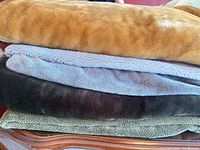 Stack of five throw blankets showing tan, light gray, charcoal, olive colors and texture
