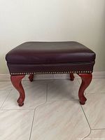 Full view of one ottoman showing leather top, nailhead trim and wood legs