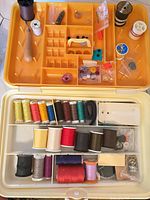 Open sewing box showing upper tray with notions and lower section with thread spools