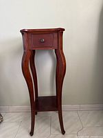 Full view of tall cherry end table showing drawer, legs, and shelf