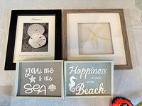 Four framed/sign pieces on table: sand dollar print, starfish shadowbox, two wood block signs