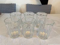 Six matching clear faceted glass tumblers on table