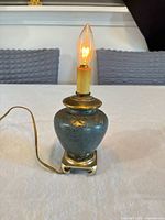 Front view of small Asian-style brass and green table lamp with lit bulb