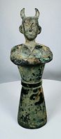 full frontal view of horned guardian figure on tapered base