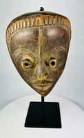 Front view of Baule mask on stand showing facial features and patina
