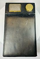 Full view of closed writing slope showing leather surface, rectangular Machinery Hall plaque, and circular gilt lid