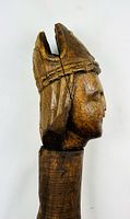 Side profile of pestle showing carved human face and headdress detail