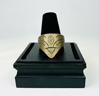 Front view of brass thumb ring on display stand showing engraved pointed face