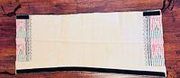 Full kilt laid flat showing cream field, geometric embroidery at ends, black side edges, tassel ties