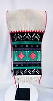 Front view of full ceremonial sash on stand showing geometric embroidery and fringe