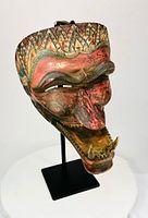Three-quarter front view of carved Cakil mask on stand