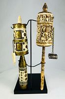 Front view of both prayer wheels on stand showing brass inlays, carved Buddha and stone counterweights