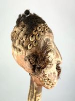 Profile of carved head showing cowrie shells and hair tufts
