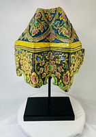 Front view of polychrome ceramic corner tile fragment on stand showing floral patterns and raised ridges