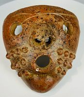 Frontal view showing stylized features, nodular cheeks, mouth and eye perforations