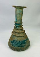 Front view of Roman turquoise glass unguentarium showing flared rim, long neck, spiral trailing, conical body, surface patina