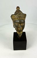 Front view of gilded bronze Buddha head on wooden base