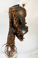 Right side view of carved wooden mask with attached fiber netting fringe