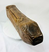 Oblique view of carved hardwood fish-form object showing head with open mouth and geometric patterns