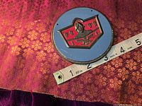 Front view of round DeSoto logo badge beside measuring tape showing ~3 in diameter