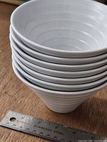 Stack of seven white ribbed conical bowls next to ruler for scale