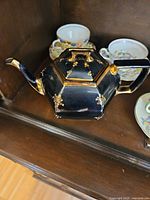 Side view of black hexagonal teapot with gold trim and multicolor dots