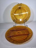 Both amber pressed glass pieces on display stand showing color and patterns
