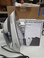 Steam iron standing upright beside manual and box