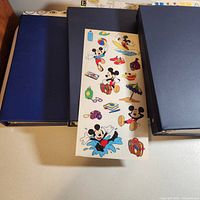 Three blue binders with a sample sheet of Mickey Mouse stickers