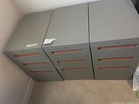 Three grey metal cabinets side by side showing drawer fronts and handles