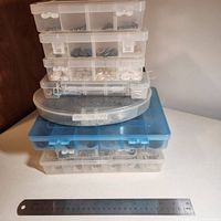 Stack of eight clear and blue-lidded plastic compartment organisers with ruler for scale