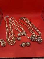 Full lot view showing three necklaces and four earrings on red background