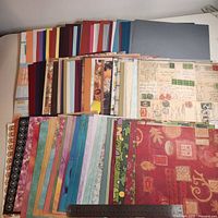 Wide view of stacked scrapbooking papers showing variety of colours and patterns with ruler for scale