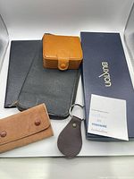 Group shot of all items: black wallet, tan cufflink case, suede key holder, keychain, Buxton box