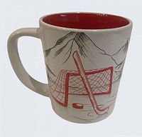 Front view showing hockey net, stick, puck and mountain scene on white mug with red interior