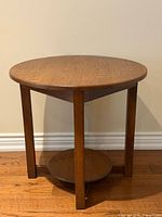 full front perspective of round oak side table showing legs and lower shelf