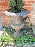 Full view of cast iron urn with evergreen against brick wall