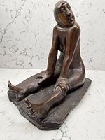 Front view of bronze seated female sculpture on marble backdrop