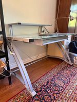 Front view of glass and metal desk showing top surface, keyboard tray, monitor shelf, and metal frame