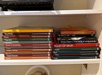 Two stacks of assorted cookbooks on shelf